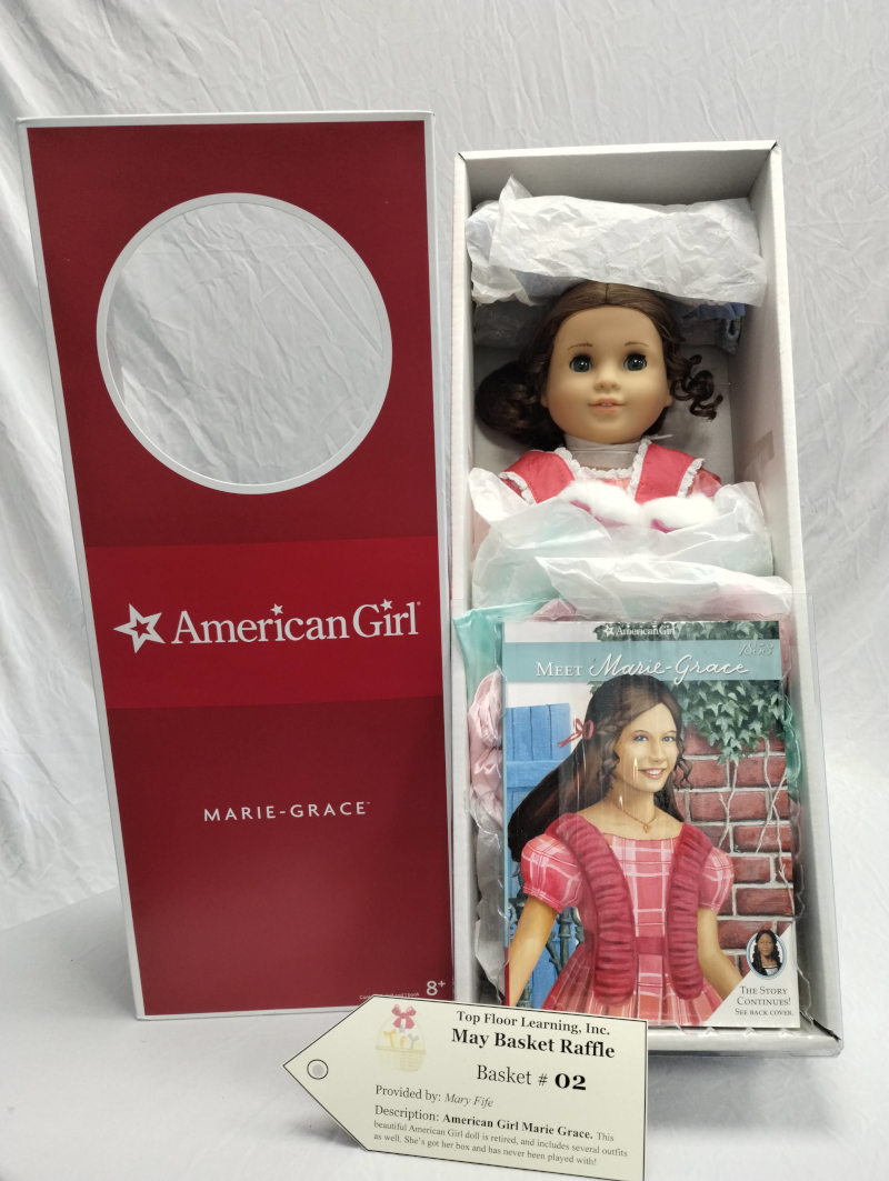 photograph of an American Girl doll in the box, with additional clothes & book in original positions