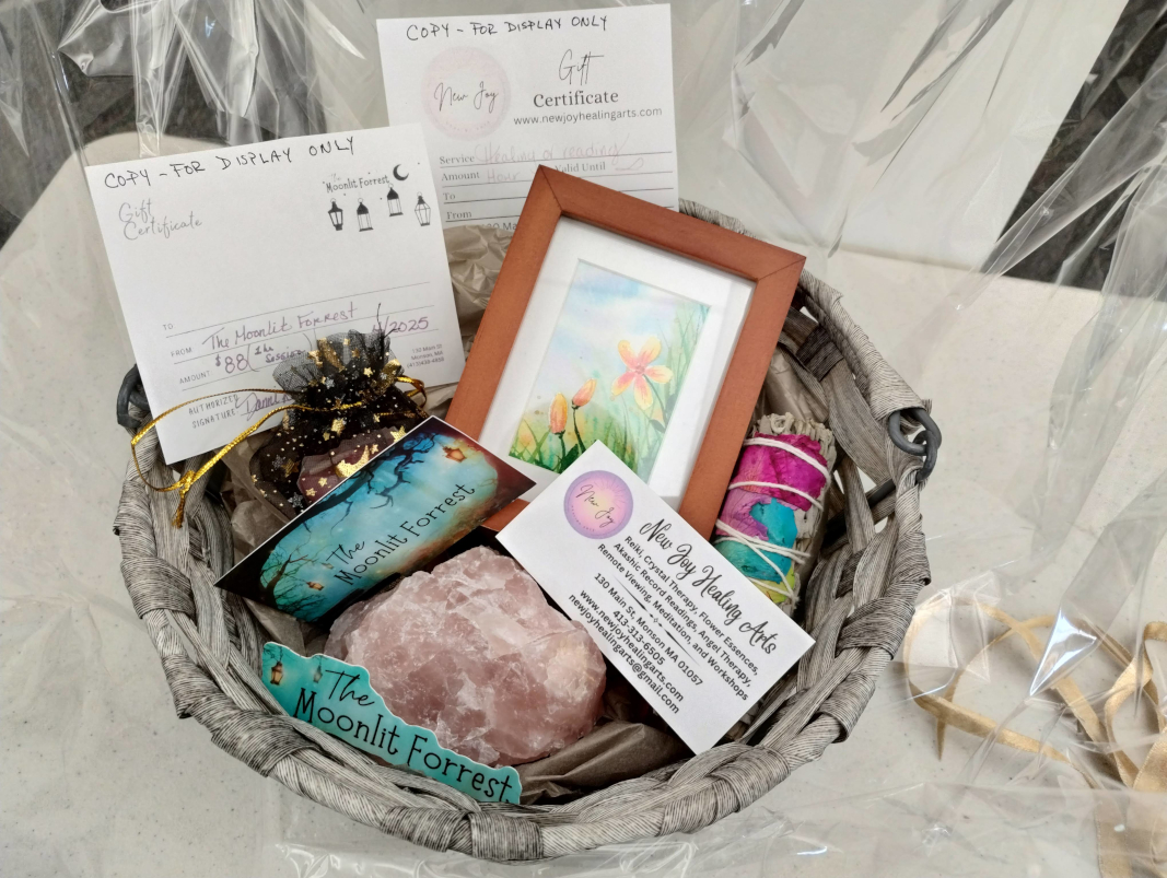 photograph of a small basket containing a large pink crystal, a wrapped sage for burning, a small framed watercolor, and a fabric pouch, as well as two gift certificates